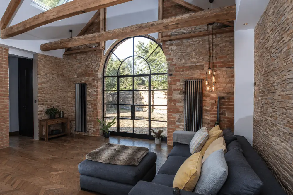Crittall doors in a rustic-modern living room with an arched black steel frame, exposed brick walls, timber beams and herringbone wood flooring