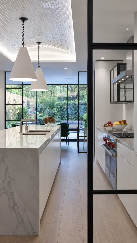 Crittall screen with a black steel frame beside a marble island in a white kitchen.